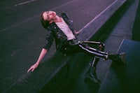 a woman in a leather jacket sitting on a ledge at night