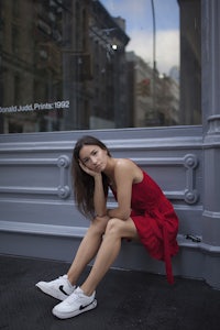 a woman in a red dress leaning against a wall